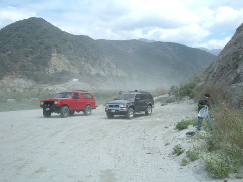 1988 Ford Bronco - Two SUVs drive on a dusty dirt road through a mountainous, arid landscape.