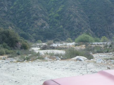 1988 Ford Bronco - A red vehicle hood is visible in the foreground of a dusty riverbed scene with mountains in the distance.