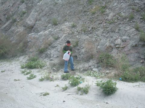 1988 Ford Bronco - A person stands in a sandy area near a rocky hillside, holding a plastic bag.