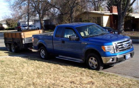 2008 Ford Crown Victoria - A blue Ford F-150 pickup truck is parked on the side of the road, hitched to a utility trailer.