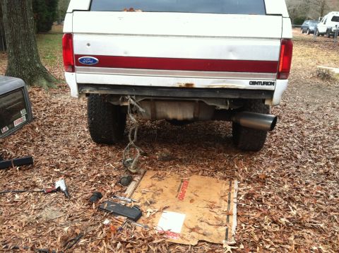 1992 Ford C-350 (Centurion Conversions) - The rear of a Ford Bronco Centurion Conversion is shown with tools and parts laid out on the ground, suggesting maintenance work.