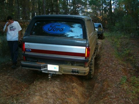 1991 Ford Bronco - This Ford Bronco is driving on a wooded trail, with another vehicle following closely behind.
