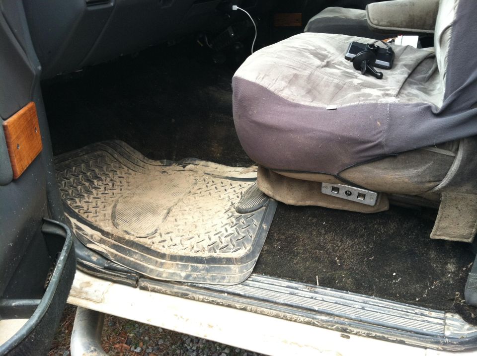 Interior shot of a dirty van or truck cab, showing a worn driver's seat and floor mats