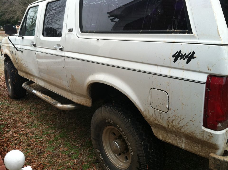 Side view of a white, four-door SUV with 4x4 decals on the rear quarter panel. It has running boards and appears to be dirty