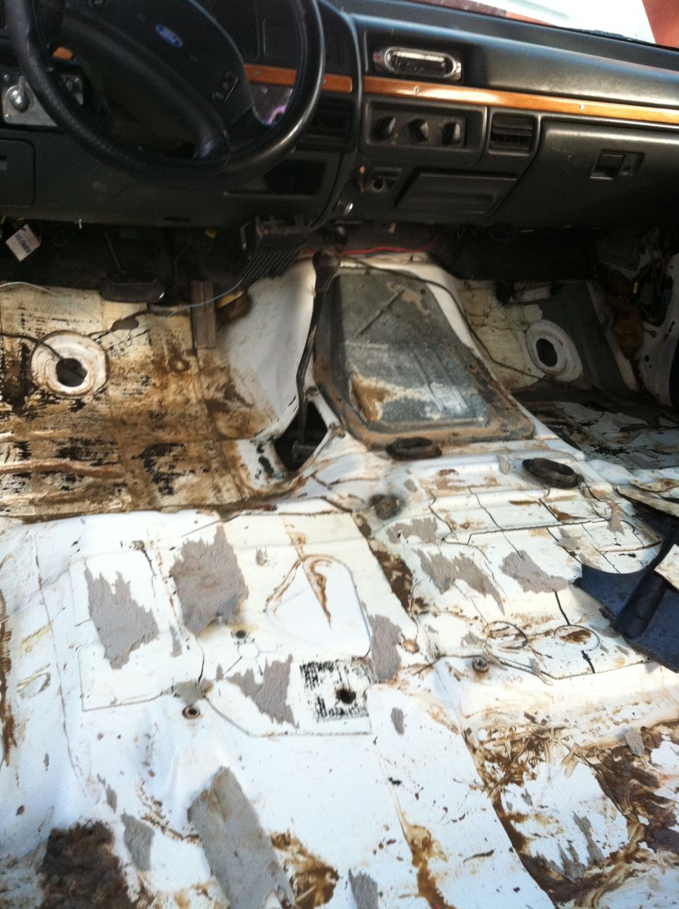 Interior floor of a truck with carpet removed, showing rust and dirt