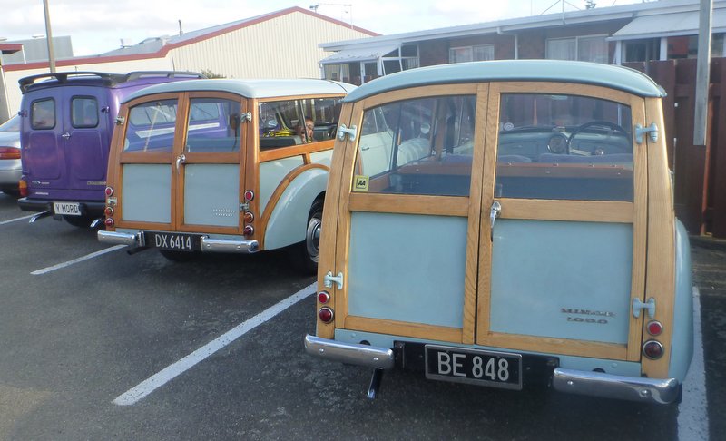 Two woodie station wagons parked side-by-side, one purple van behind them
