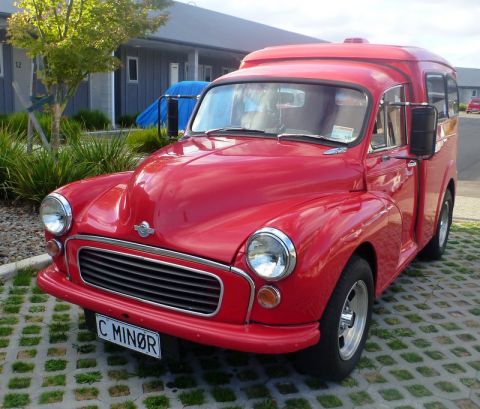 1969 MINI Cooper - A bright red van with a custom license plate is parked outside a building.