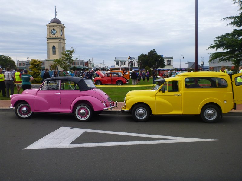 Pink convertible and yellow van parked side-by-side on a street, with a clock tower in the background
