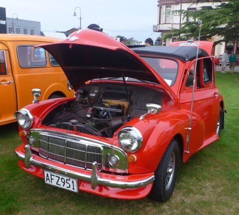 1969 MINI Cooper - A red Morris Minor 1000 is displayed with its hood open, parked on grass next to an orange van.