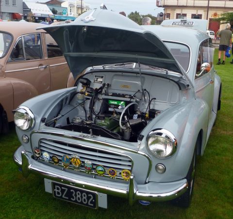 1969 MINI Cooper - Morris Minor 1000 at an outdoor car show, engine bay exposed and grille decorated with multiple badges.