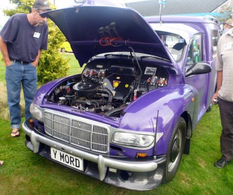 1969 MINI Cooper - A purple van with its hood open, revealing the engine, is displayed outdoors with onlookers.