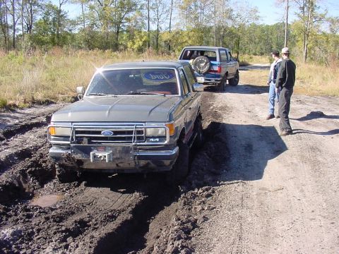 1991 Ford Bronco - Two Ford Broncos on a muddy trail, one is stuck.