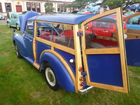 1969 MINI Cooper - A blue woodie station wagon is parked on grass with its rear door open, alongside other vehicles.