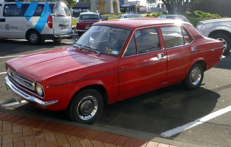 Red sedan parked next to a white van and a silver SUV