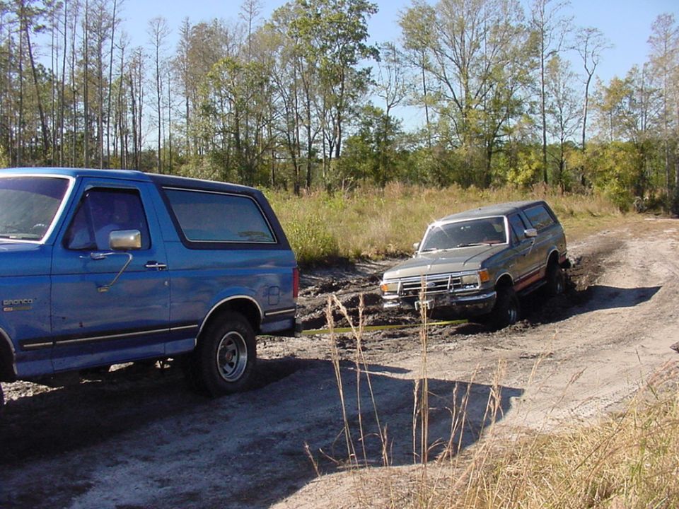 Blue Bronco pulling a stuck gray Bronco out of mud