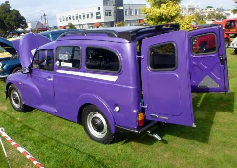1969 MINI Cooper - A purple van is parked on a grassy field with its rear doors open, showing a glimpse of the interior.