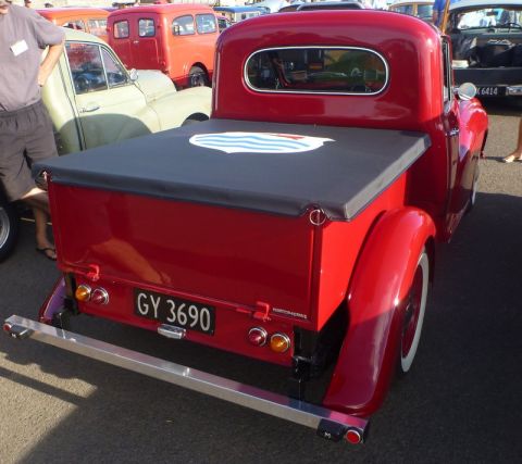 1969 MINI Cooper - Rear view of a red pickup truck with a tonneau cover, parked outdoors with other vehicles.
