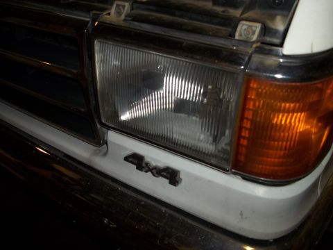 1990 Ford Bronco - Close-up of the 1990 Ford Bronco's front headlight and 4x4 emblem.