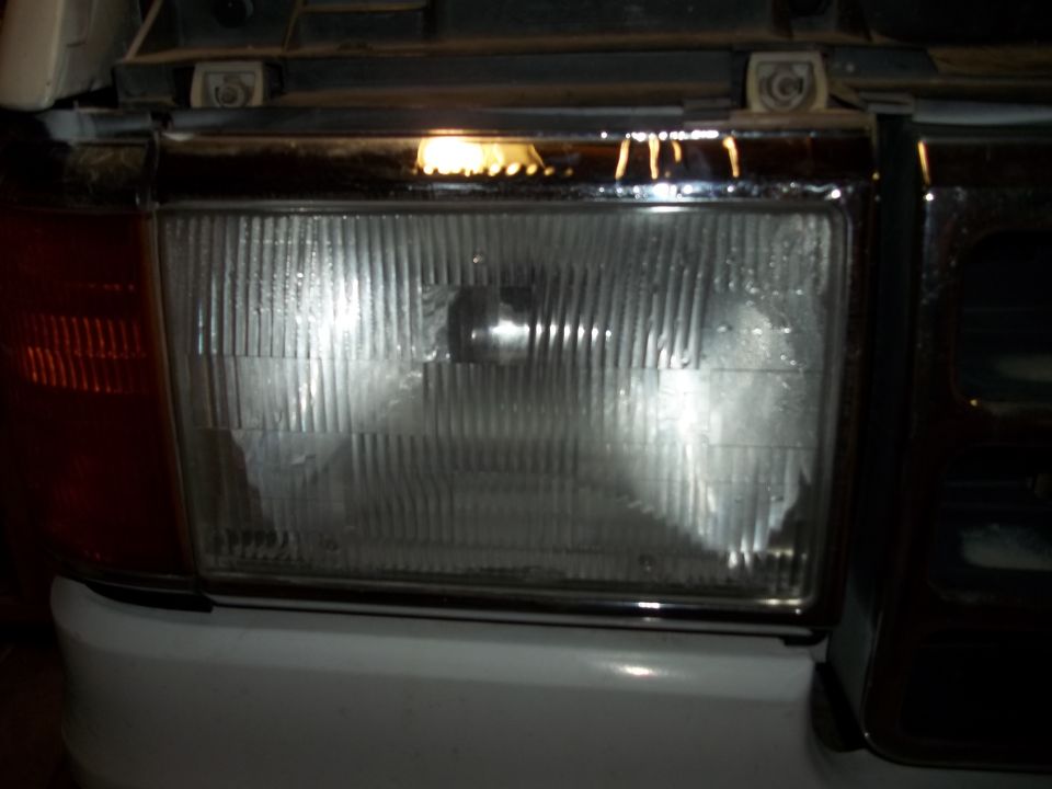1990 Ford Bronco headlight assembly with chrome trim and vertical grille lines