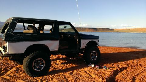 1994 Ford Bronco - A lifted Ford Bronco sits on a sandy shore with a calm lake and distant mesas under a clear blue sky.