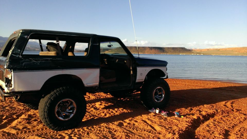 Lifted Ford Bronco parked on a sandy beach next to a lake