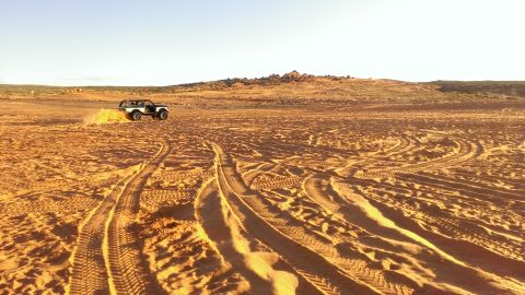 1994 Ford Bronco - A white 1994 Ford Bronco kicks up sand as it drives across a desert landscape.