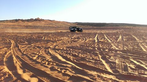 1994 Ford Bronco - A vehicle navigates a sandy terrain under a clear blue sky, leaving behind numerous tire tracks.