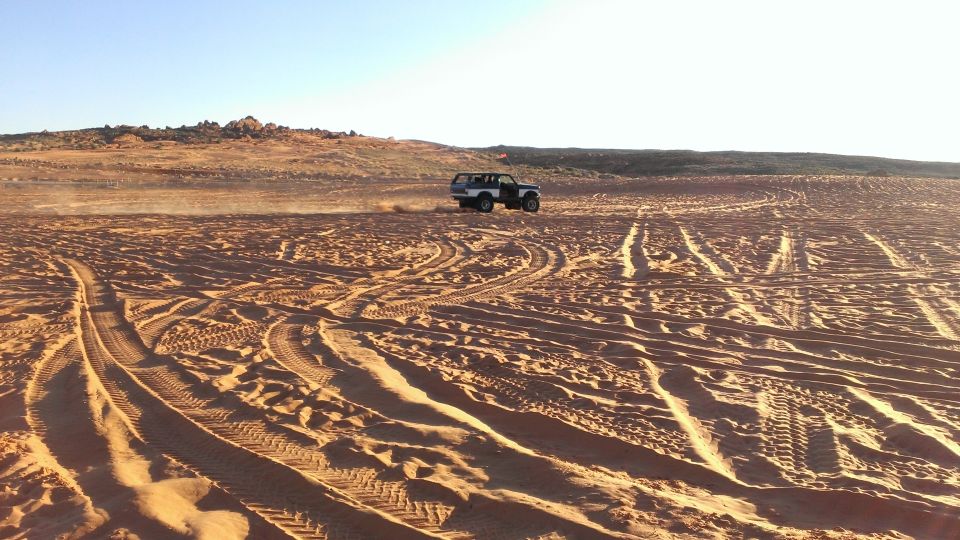 SUV kicking up sand while driving across a desert landscape with tire tracks visible