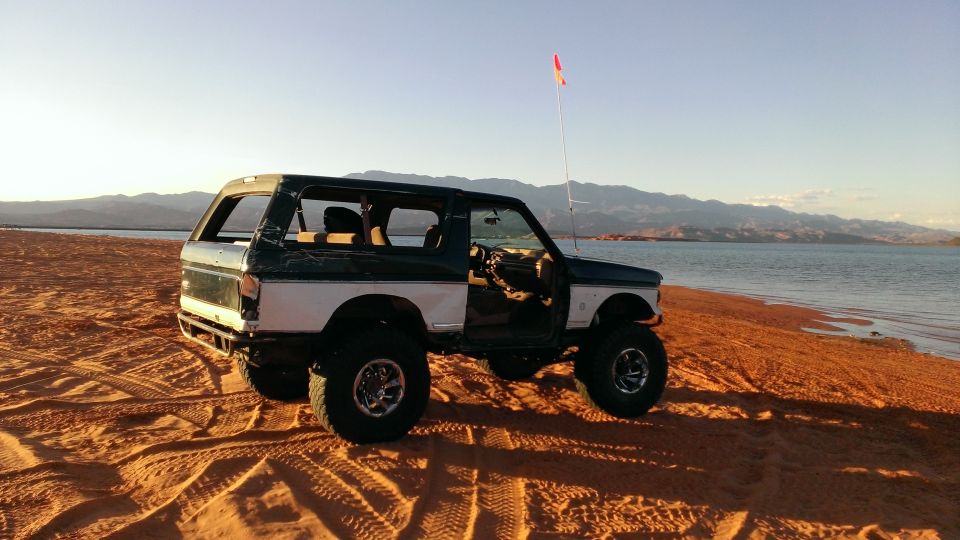 Two-tone green and white Ford Bronco with lifted suspension parked on a sandy beach