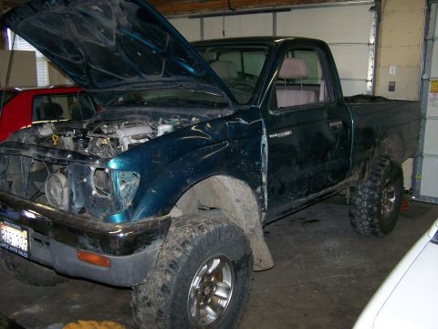 1988 Suzuki Samurai - A dark green pickup truck sits in a garage with its hood open, revealing the engine compartment.