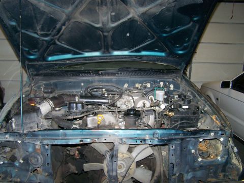 1988 Suzuki Samurai - The engine bay of a teal SUV is shown with the hood open, and another vehicle is visible to the right.