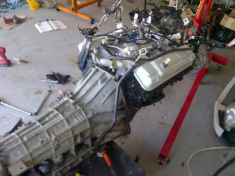 1994 Ford Bronco - Vehicle engine and transmission assembly suspended by chains, resting on the garage floor with tools nearby.