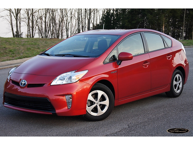 Red Toyota Prius, three-quarter front view, parked on asphalt with trees in background