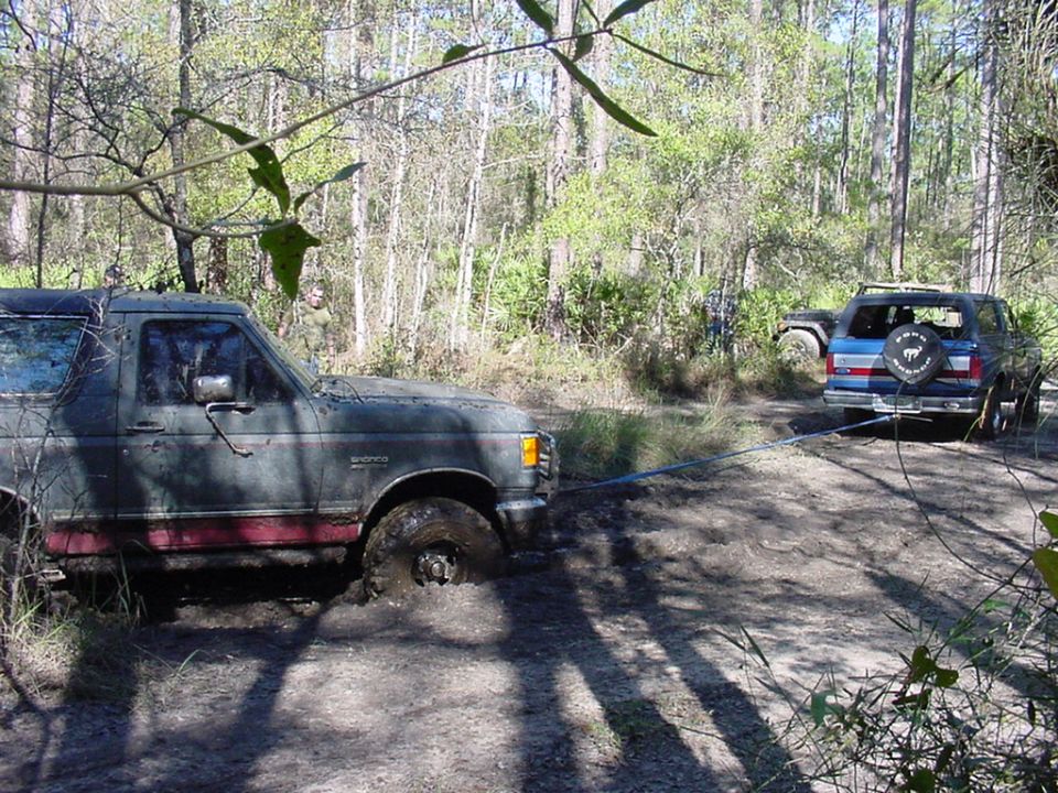 1991 Ford Bronco stuck in mud, being towed by blue SUV