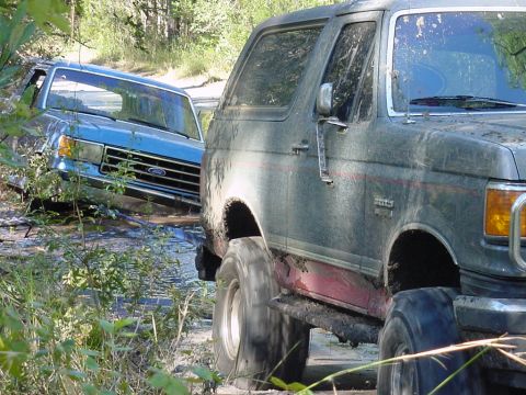 1991 Ford Bronco - Two Ford trucks are stuck in the mud on a trail.