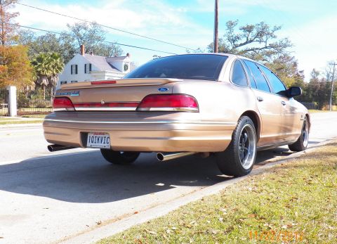 1993 Ford Crown Victoria - Rear view of a gold sedan with aftermarket wheels and a spoiler. The license plate is visible.