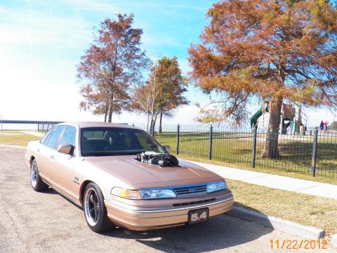 1993 Ford Crown Victoria - This modified 1993 Ford Crown Victoria features an exposed engine, parked near a playground.