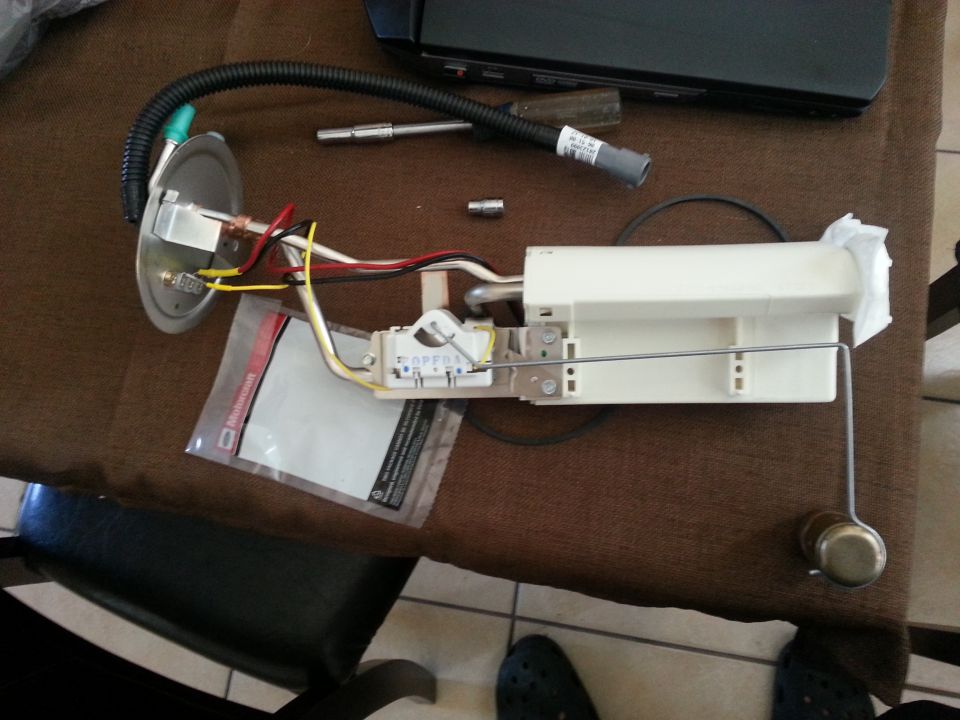 Fuel pump assembly with wires and hose on a brown surface. A white plastic housing is visible
