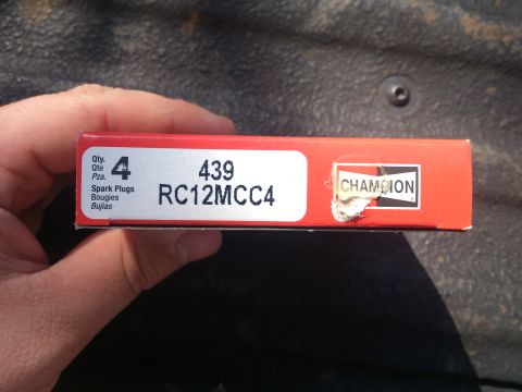 2004 Dodge 1500 - A box of Champion spark plugs is held in a hand against a dark, textured background.