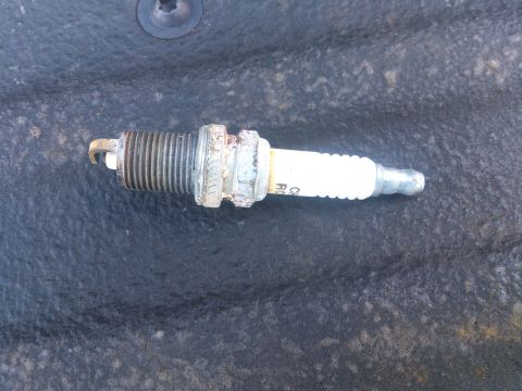 2004 Dodge 1500 - A used spark plug, possibly from a Dodge 1500, is shown against a dark, textured background.