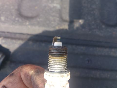 2004 Dodge 1500 - A single spark plug is shown, held by a hand with grease stains.