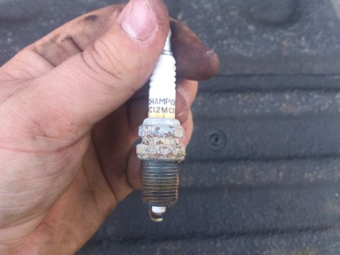2004 Dodge 1500 - A close-up shows a Champion spark plug held in a dirty hand, with visible wear on the electrode.