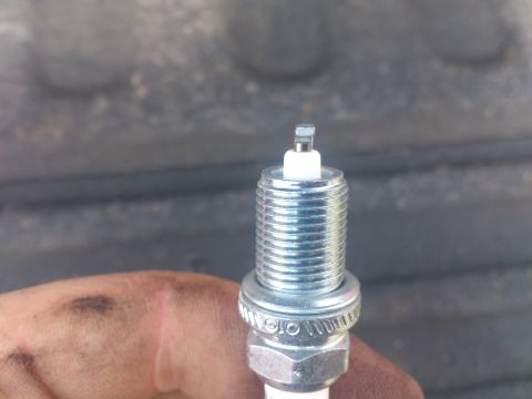 2004 Dodge 1500 - A single spark plug is shown, held by a hand with dirt smudges. The background is out of focus.