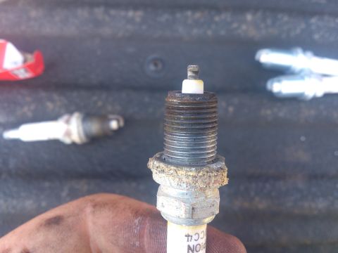 2004 Dodge 1500 - A used spark plug is held in focus, with other spark plugs blurred in the background.