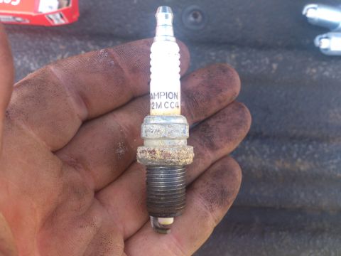 2004 Dodge 1500 - A dirty hand holds a used Champion spark plug, showing signs of wear and tear.