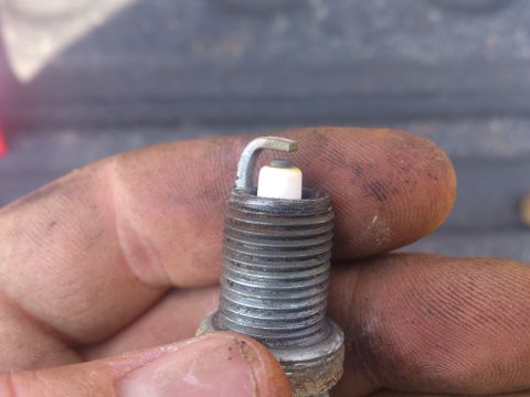 2004 Dodge 1500 - A close-up view of a spark plug being held by a person's dirty fingers.