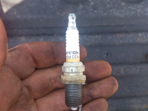 2004 Dodge 1500 - A Champion spark plug, labeled 2M CC4, is held in a hand with dirt on it. The background is out of focus.