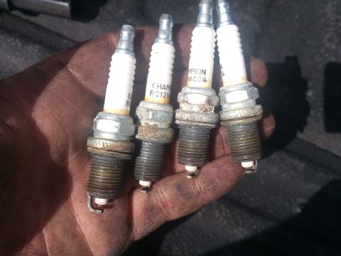 2004 Dodge 1500 - Four used Champion spark plugs, some showing wear and carbon buildup, are held in a hand.