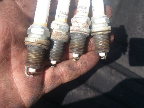 2004 Dodge 1500 - A hand displays four worn Champion spark plugs, showing signs of use and wear.