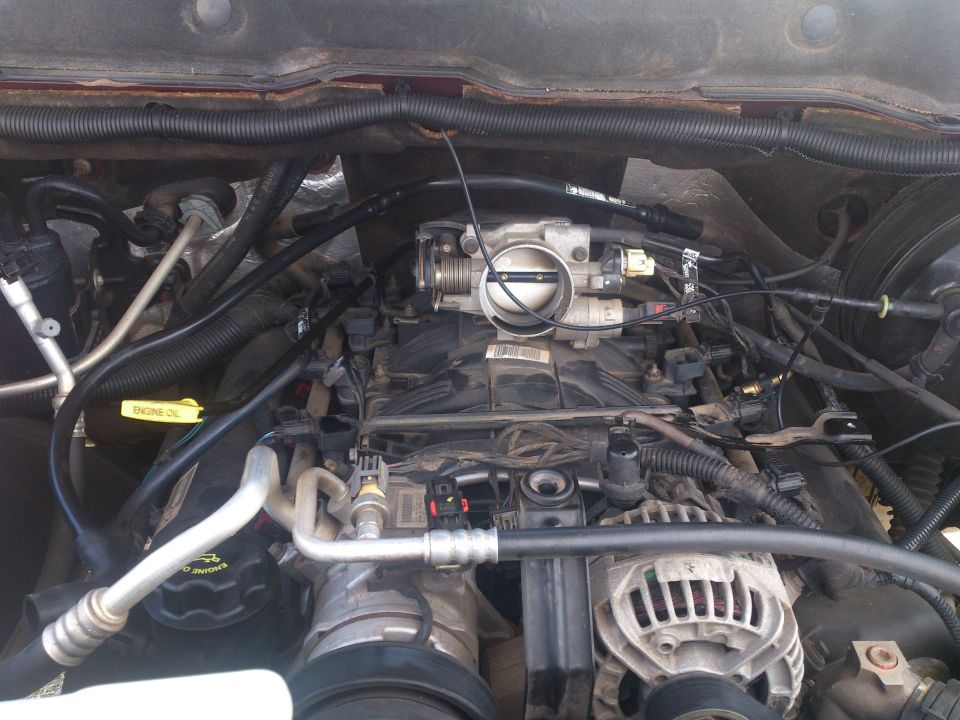 Engine bay of a 2004 Dodge 1500 showing the throttle body, alternator, and various hoses